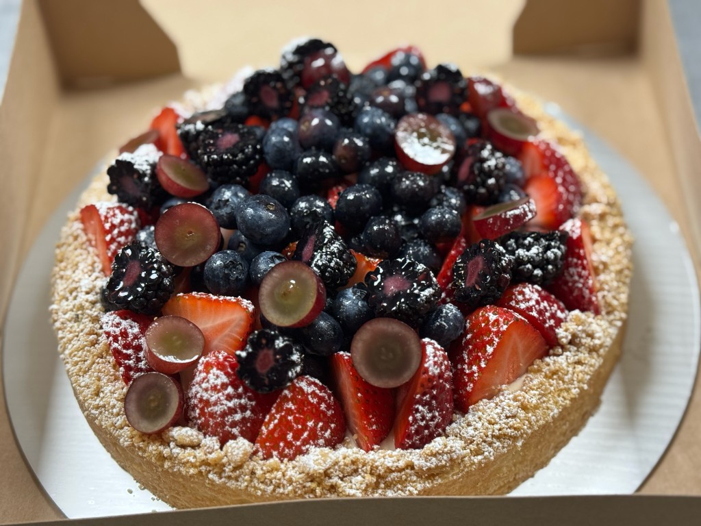 A fresh fruit tart topped with strawberries, blueberries, blackberries, and grapes, dusted with powdered sugar.